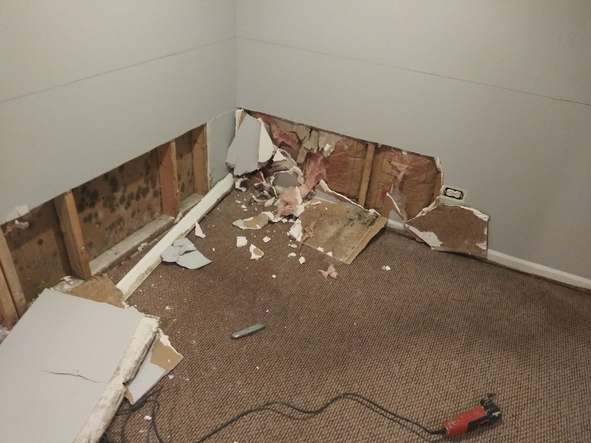 A room with a hole in the wall and a drill on the floor