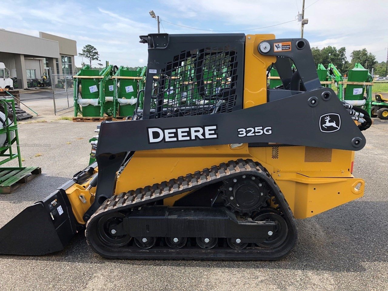 John Deere 325G compact track loader, black and yellow, parked outdoors on pavement.
