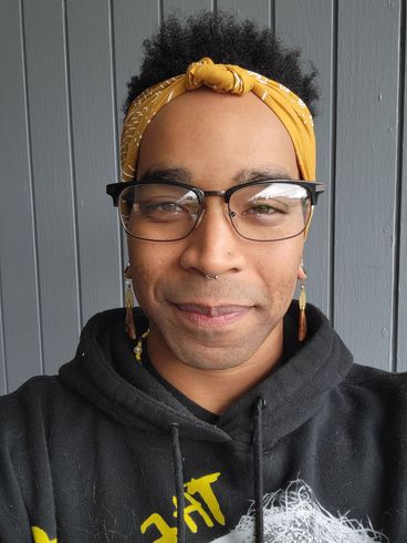 A man with dreadlocks and a bandana on his head smiles for the camera