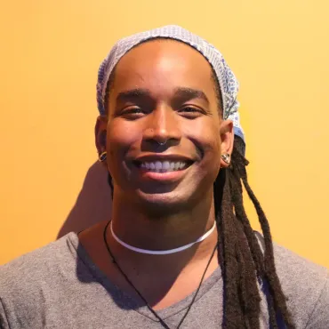 A man with dreadlocks and a bandana on his head smiles for the camera