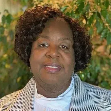 A woman with curly hair is wearing a jacket and smiling for the camera.