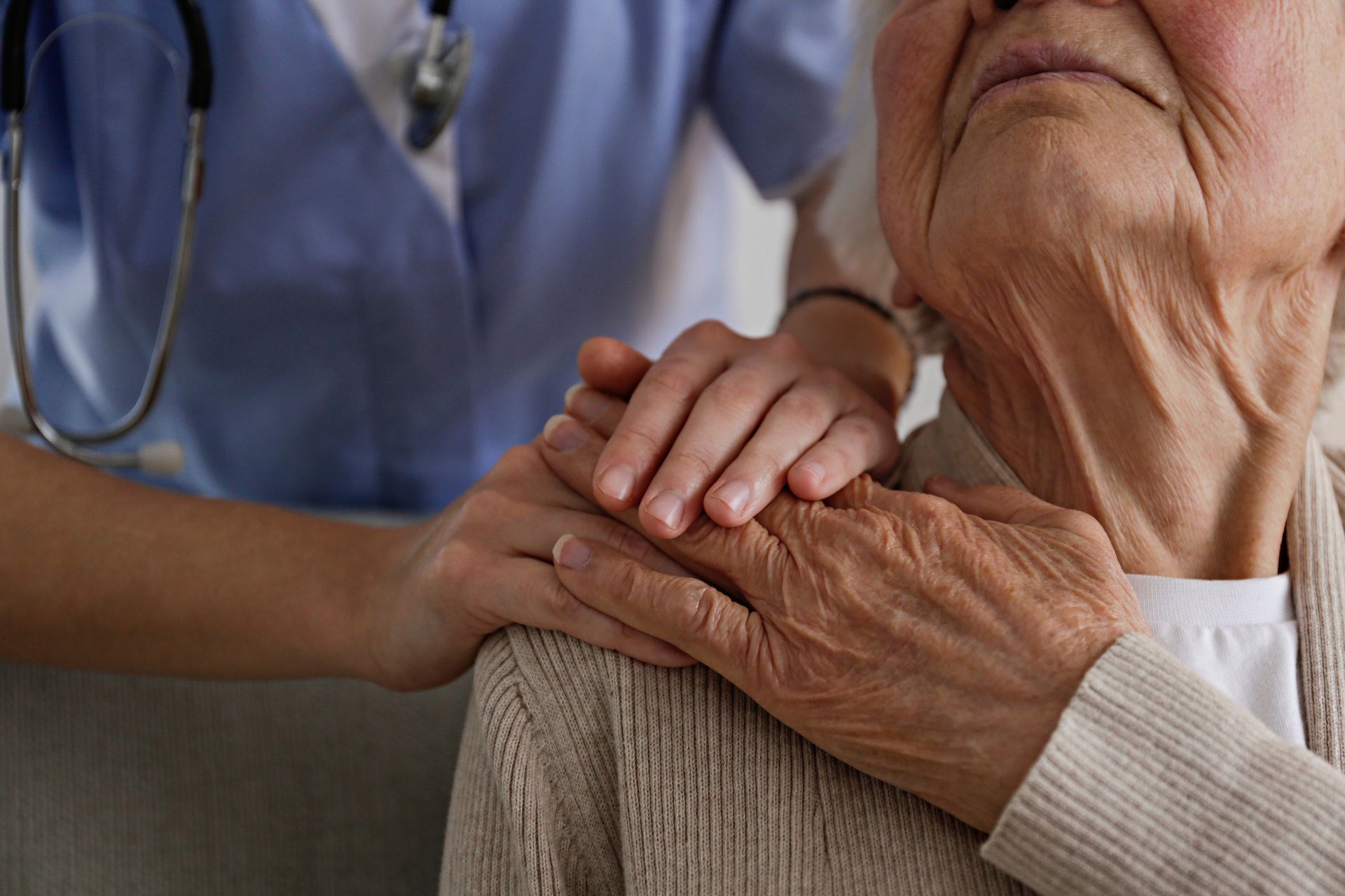 A healthcare worker comforting an elderly person with a hand on their shoulder.
