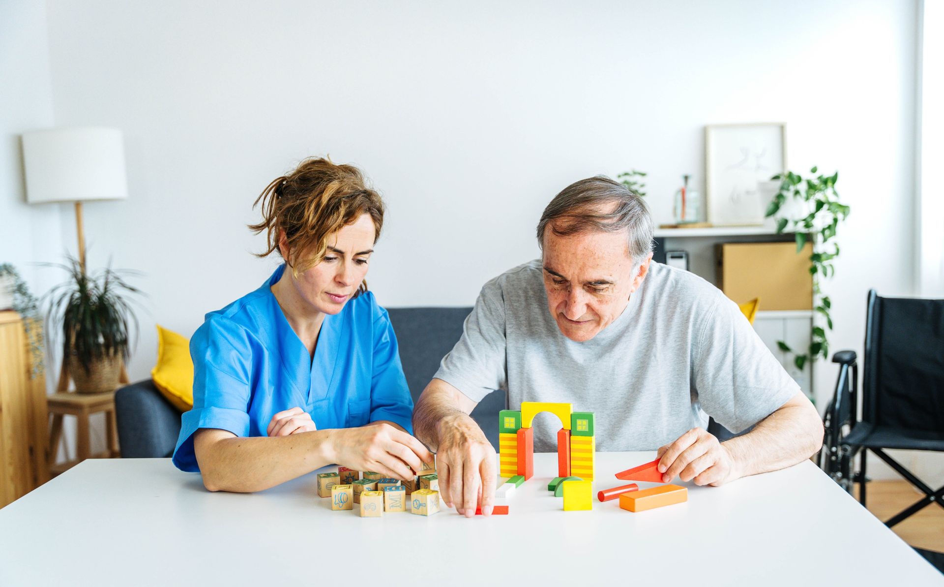 A healthcare worker and a person play with colorful blocks at a table.
