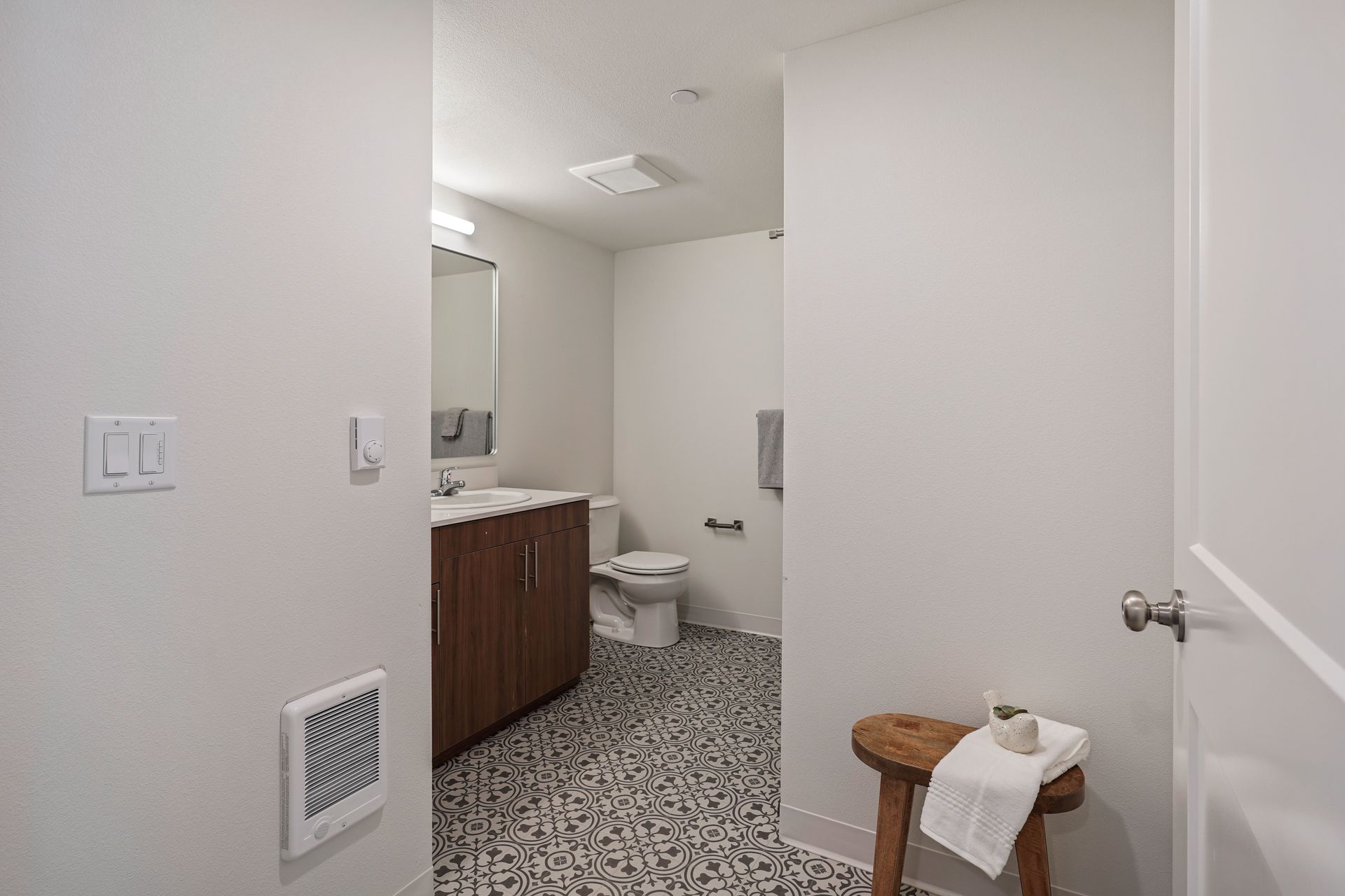 A bathroom with a toilet , sink , mirror and stool.