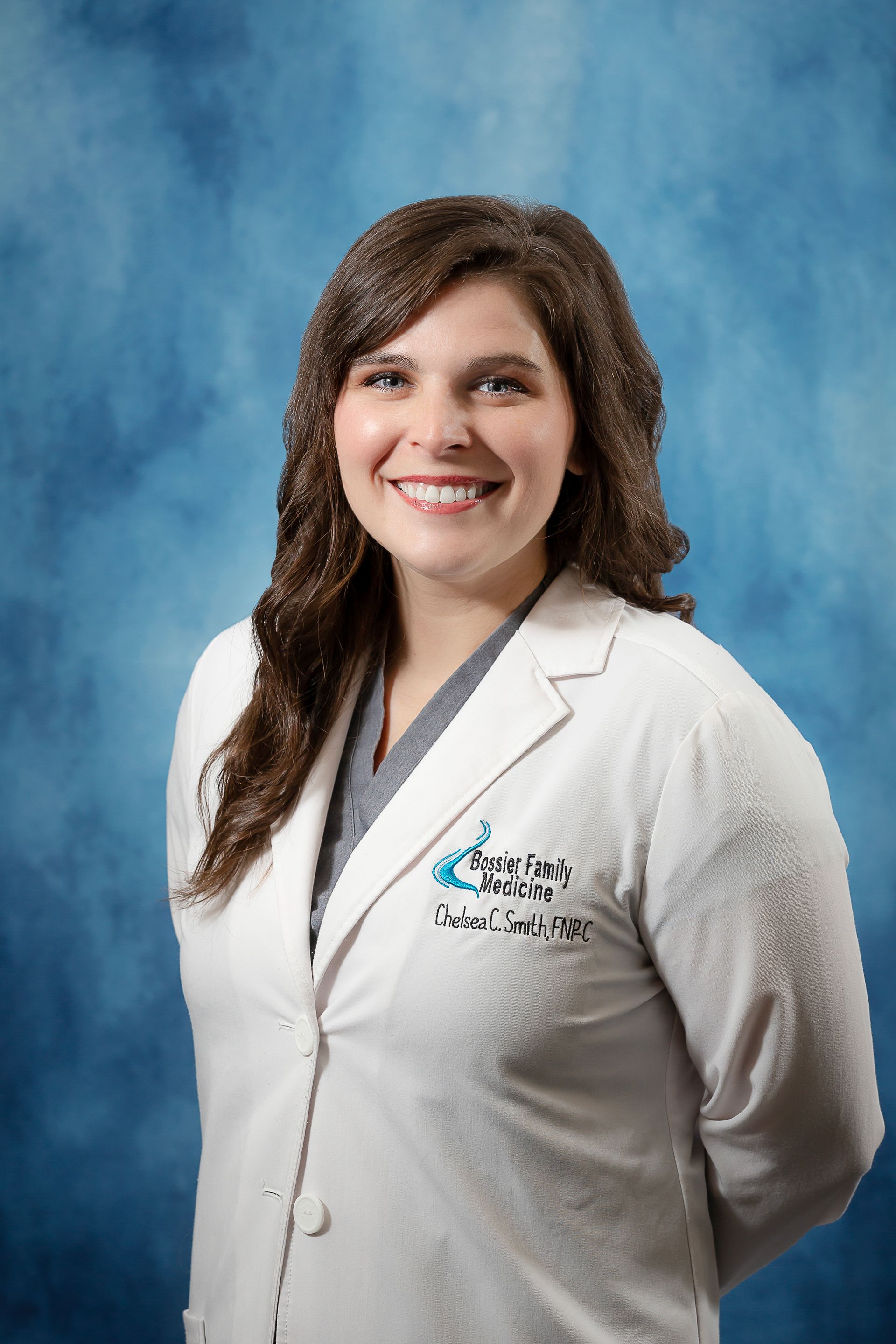 A woman in a white lab coat is smiling and standing in front of a blue background.