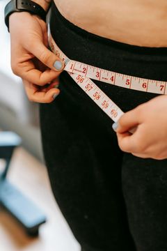 A woman is measuring her waist with a tape measure.