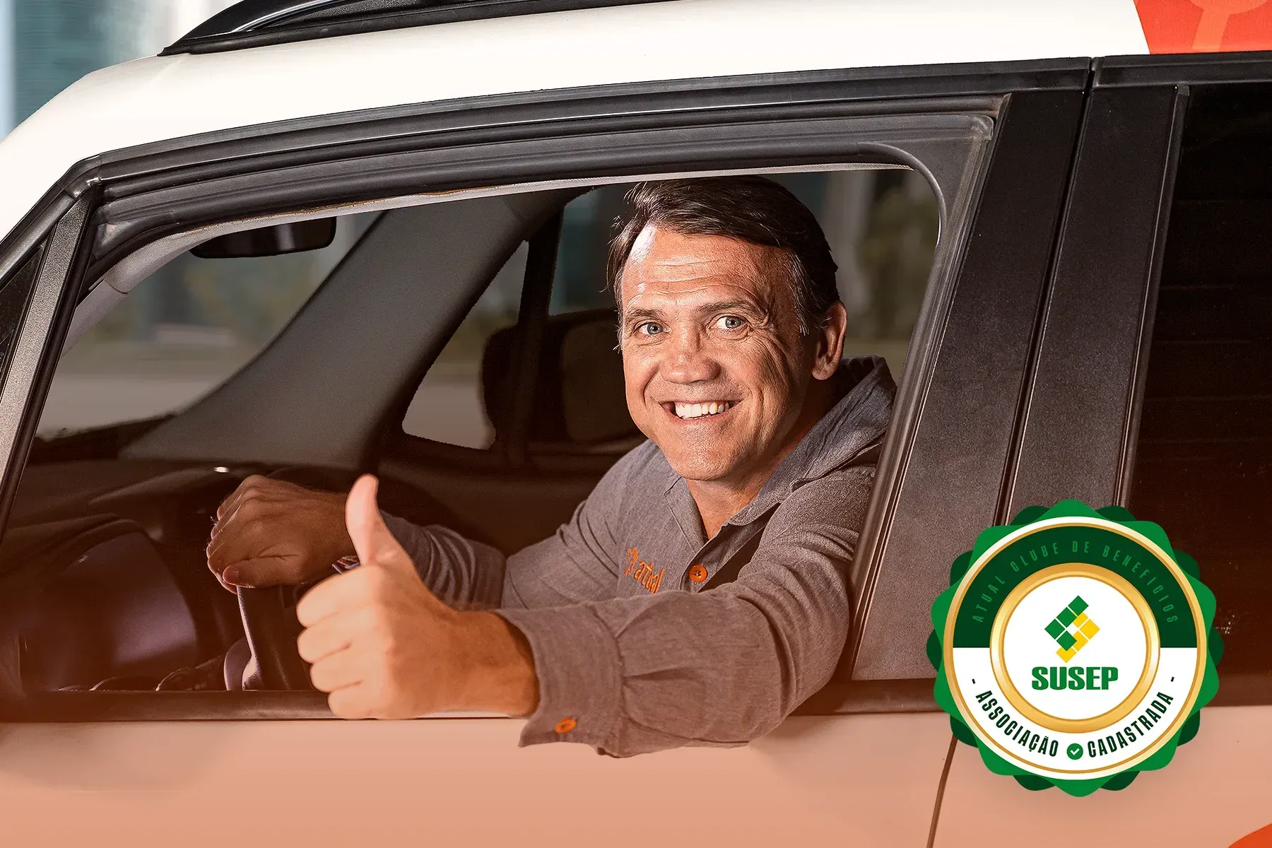 Motorista sorridente fazendo sinal de positivo dentro de um carro, com um logotipo verde e branco no canto.