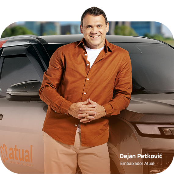 Homem sorridente com camisa laranja em pé na frente de um carro com o logotipo da Mutual e a inscrição 