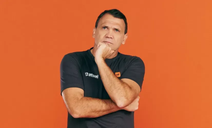 Homem de camisa preta posando pensativamente contra um fundo laranja.