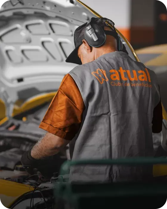 Mecânico de uniforme cinza e laranja trabalhando no motor de um carro em uma garagem.