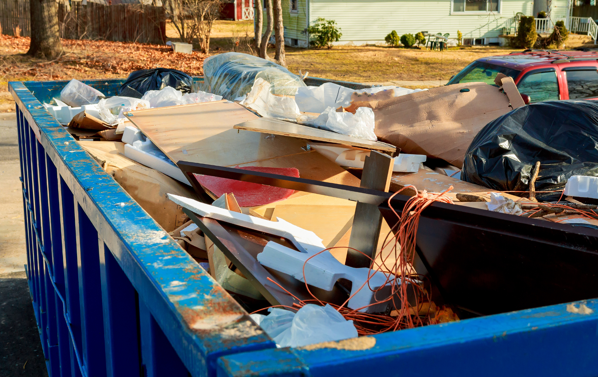 Blue dumpster filled with construction debris, cardboard, and trash.