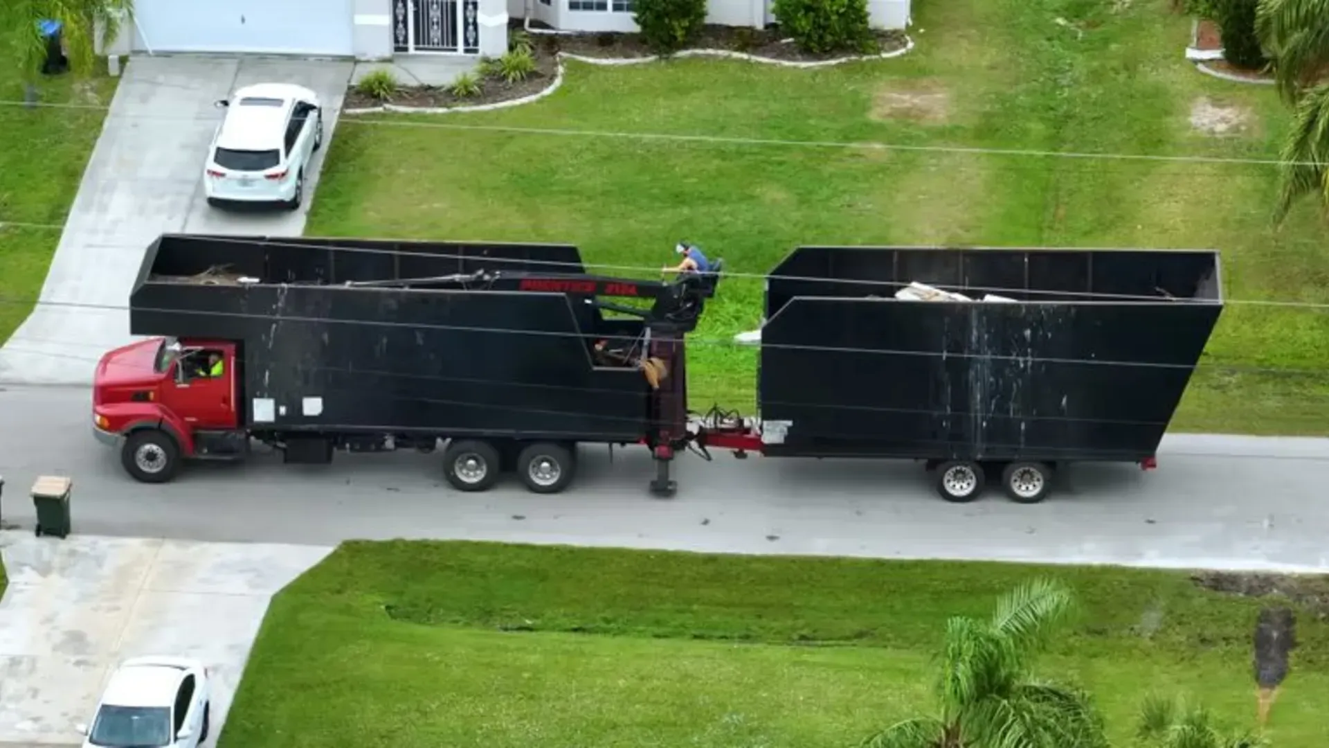 Red and black garbage truck with two containers on a residential street.