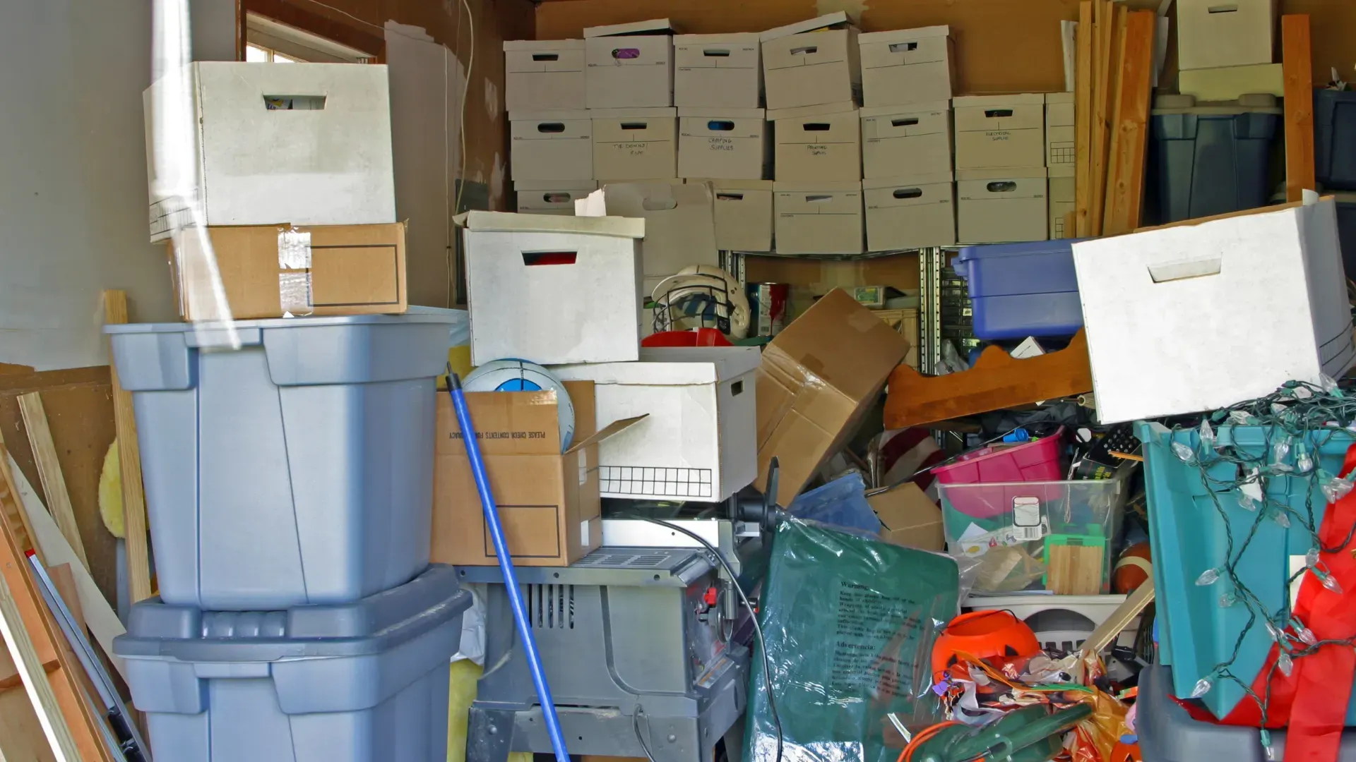 Cluttered garage with stacked storage boxes, bins, and various items.