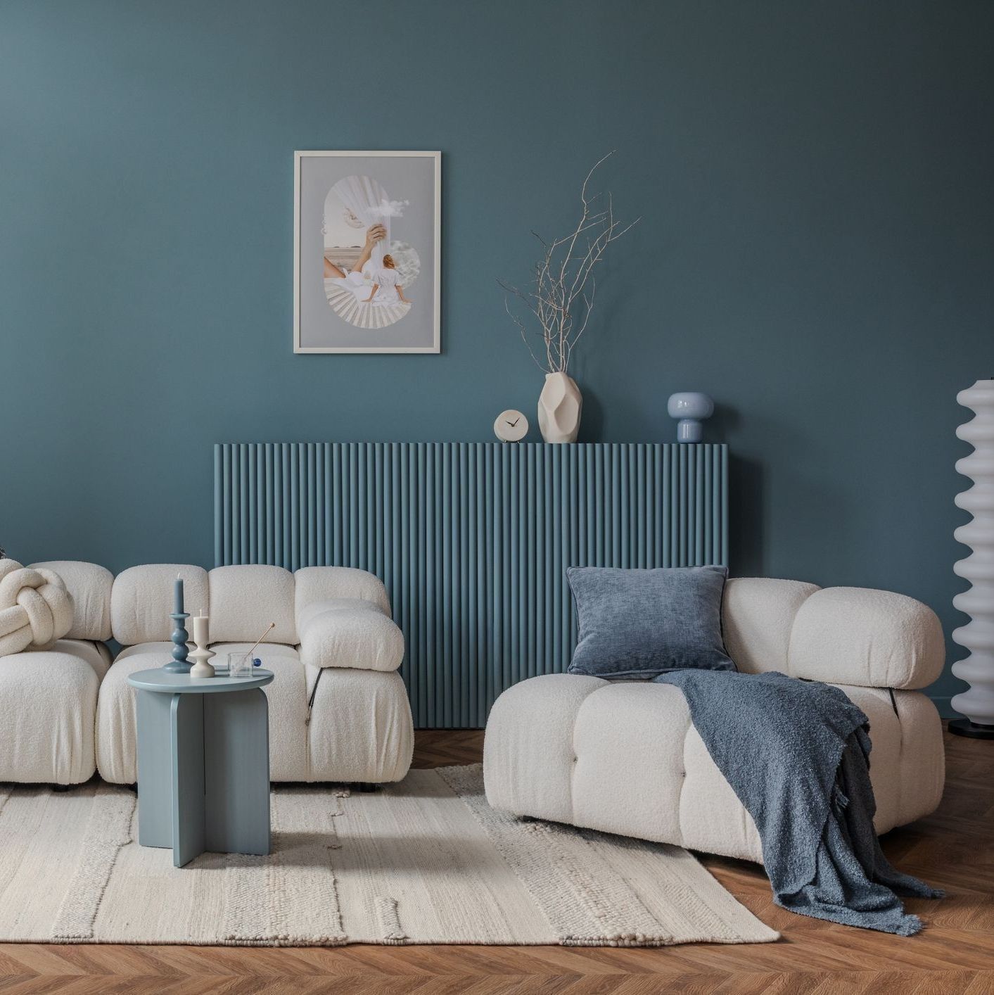 Soggiorno dallo stile minimalista e delicato, con parete blu-verde, poltrone color crema, pouf rotondo e tappeto dalla texture particolare.