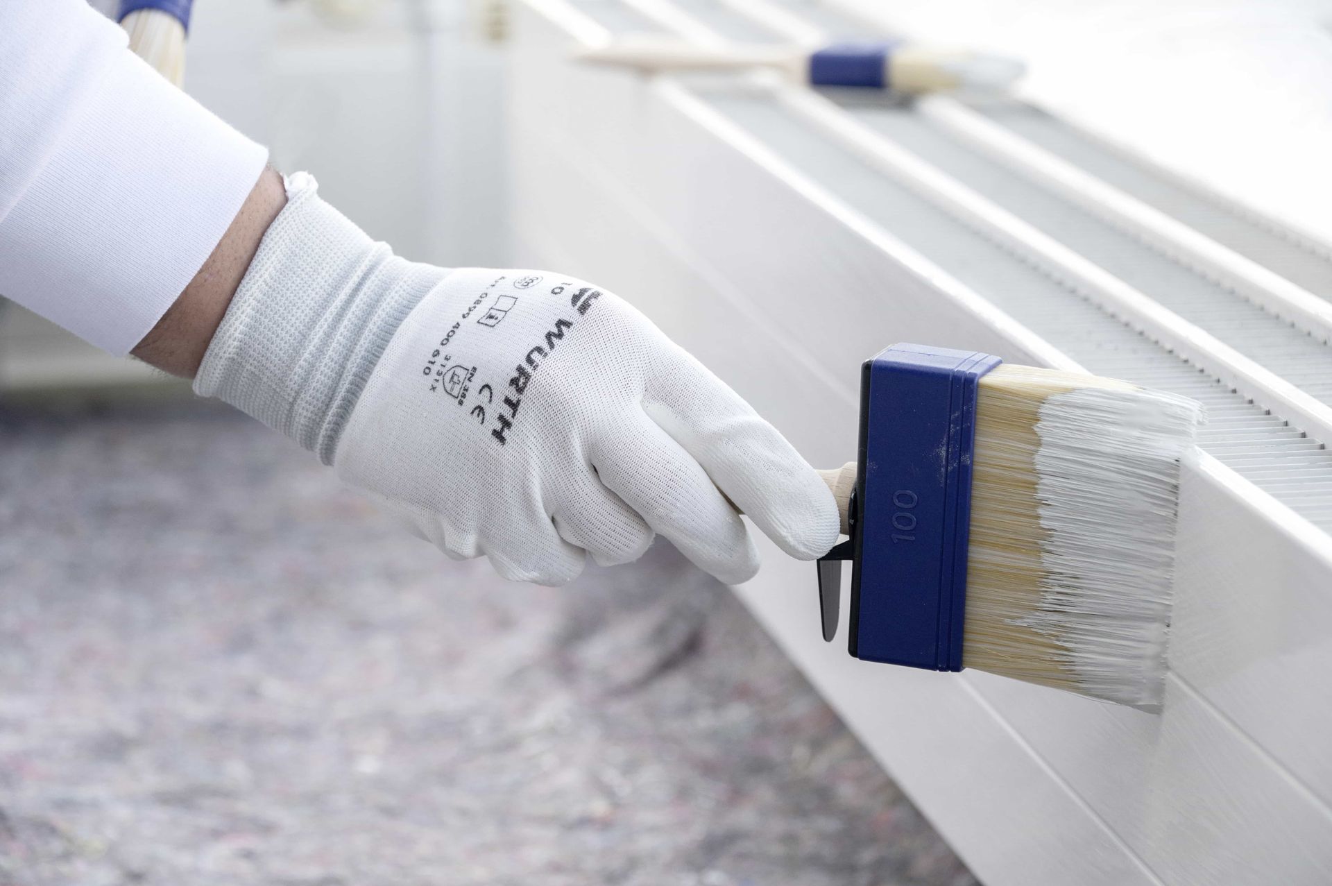 Mano guantata che dipinge una recinzione bianca con un pennello blu all'aperto