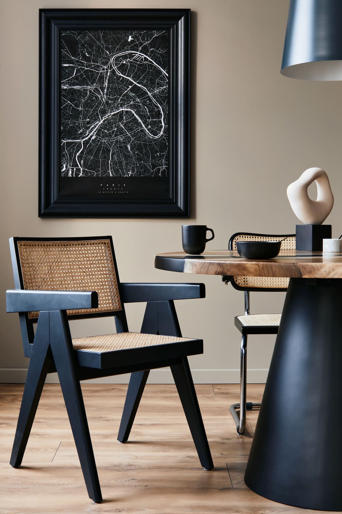 Angolo pranzo moderno con sedie nere, tavolo rotondo, quadri alle pareti e pareti beige.