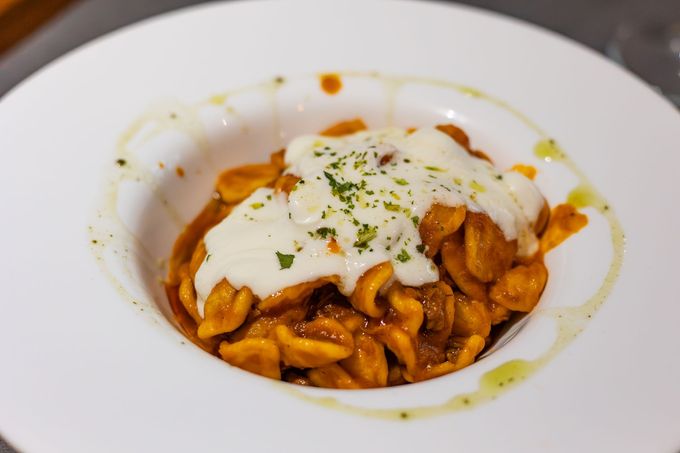 Pasta al sugo di pomodoro con formaggio fuso ed erbe aromatiche in una ciotola bianca.