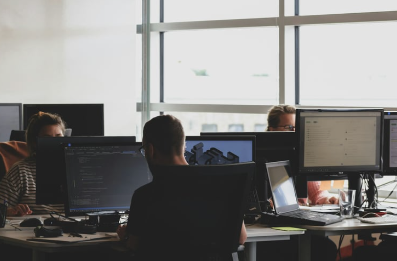 People working at computers in an office with large windows.