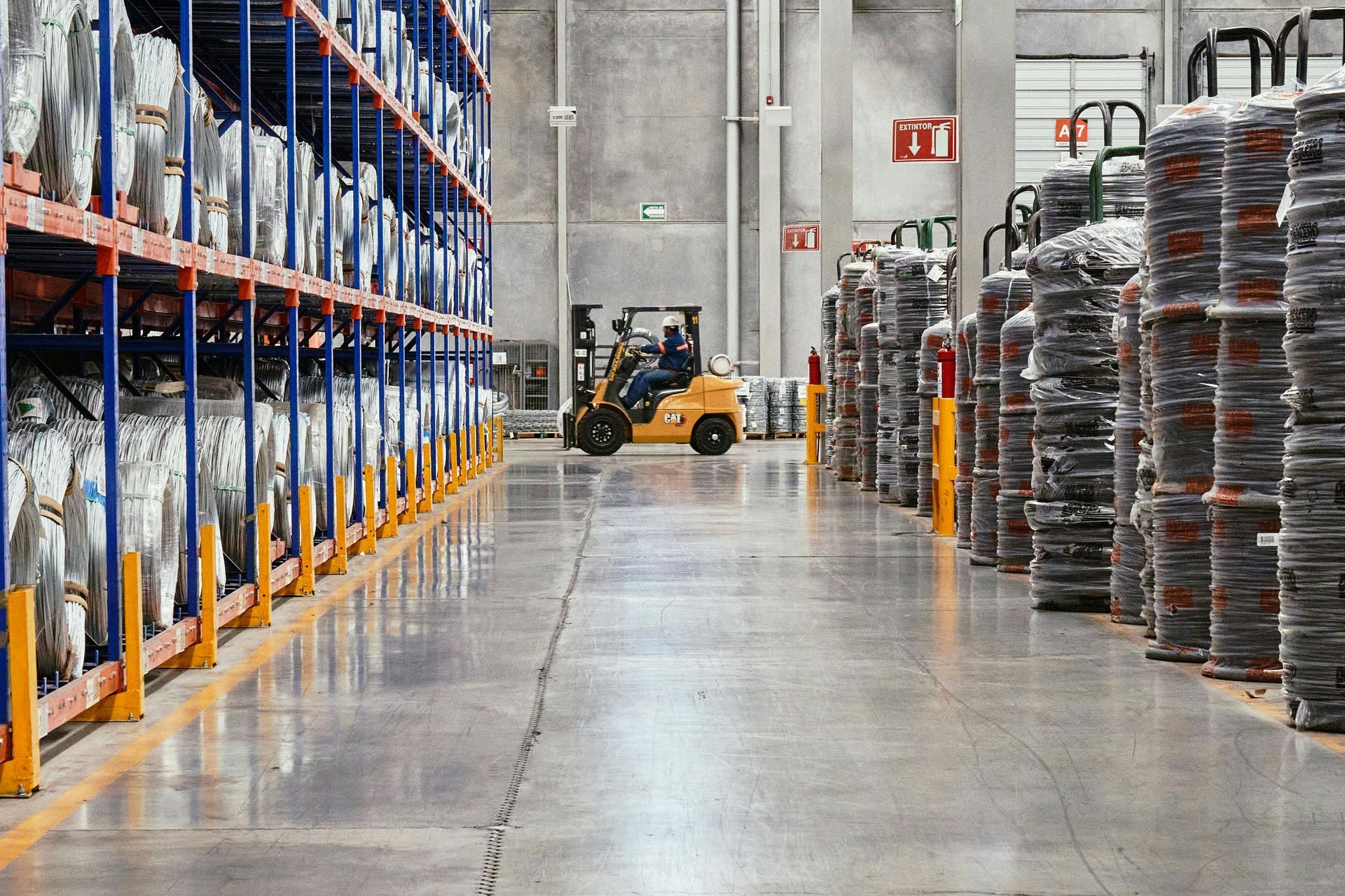 Warehouse aisle with stacked pallets, shelves, and a forklift on a polished concrete floor