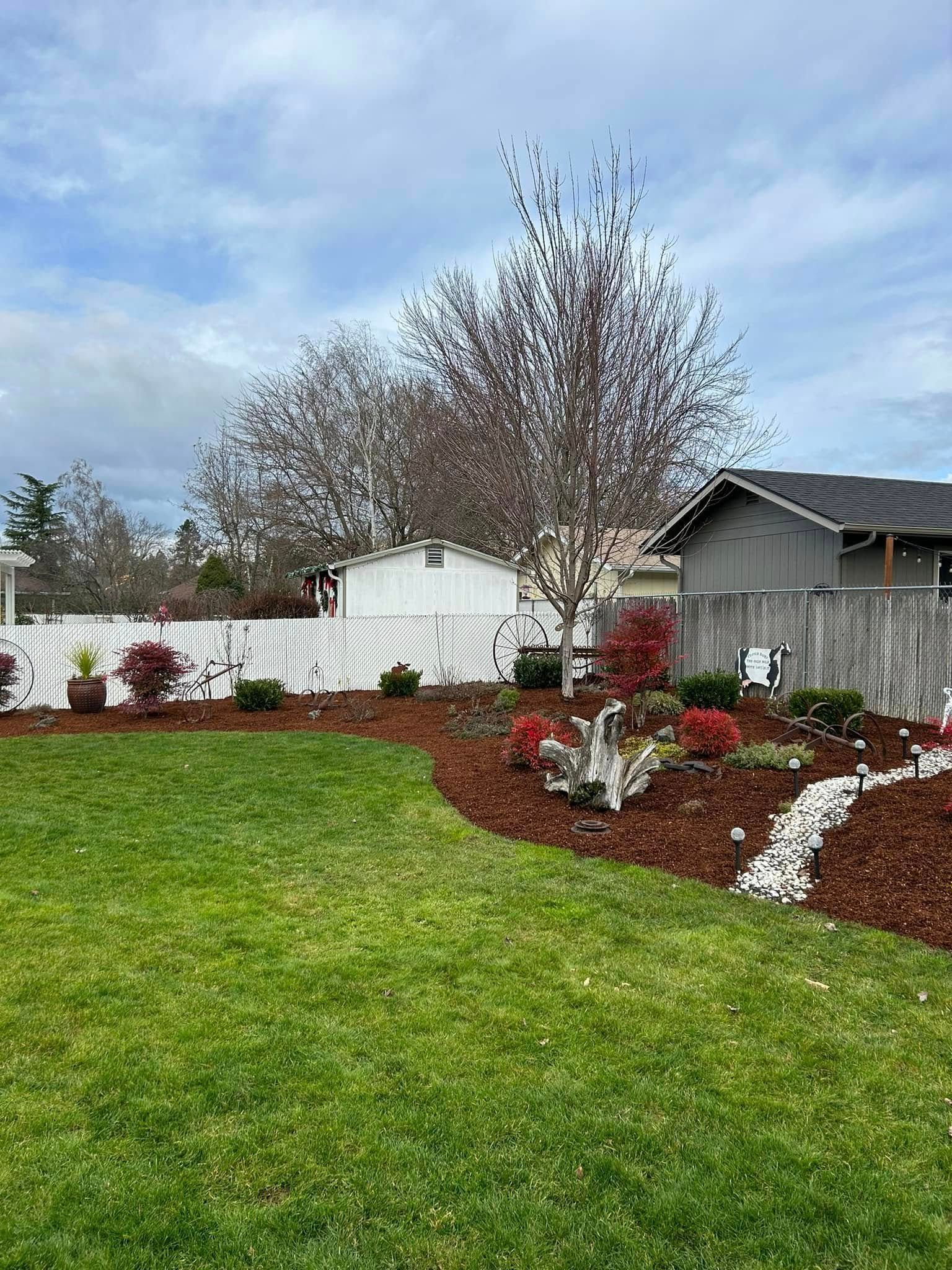 A lush green yard with a white fence and a house in the background.