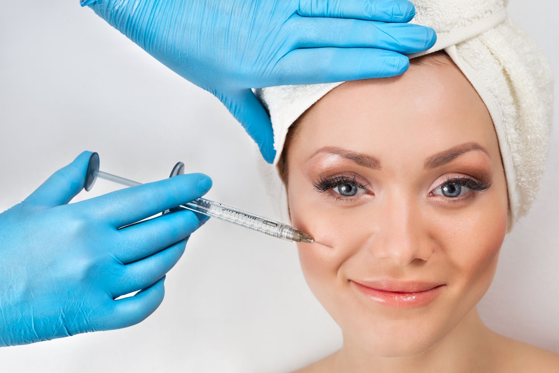 A woman with a towel wrapped around her head is getting a botox injection.