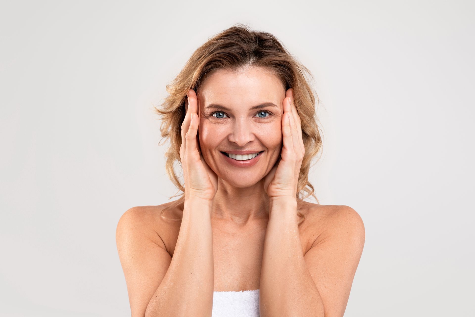 Woman with hands on face, smiling, against a light background.