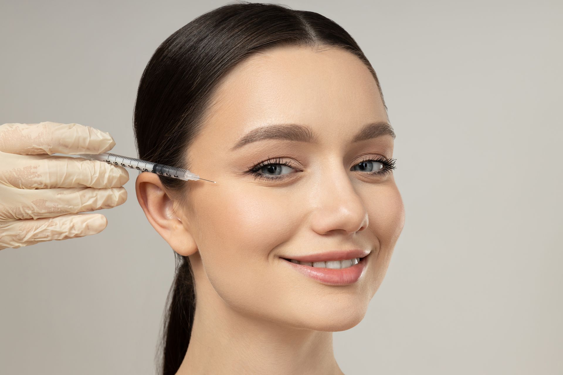 A person receiving an injection near their eye; smiling, light skin, neutral background.