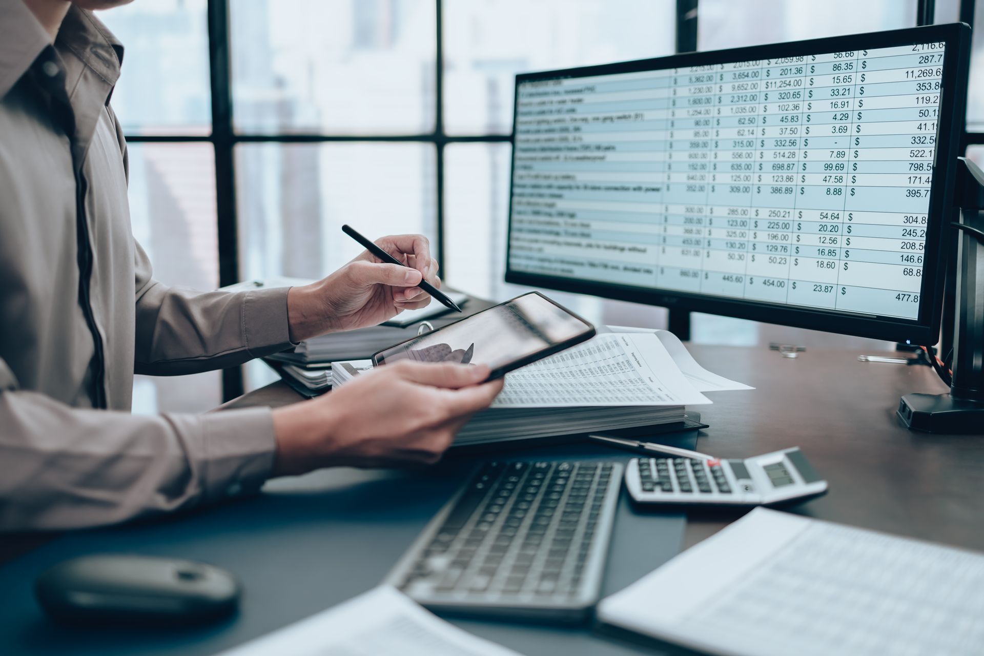An accountant working on a desk and using a tablet to track business costs.
