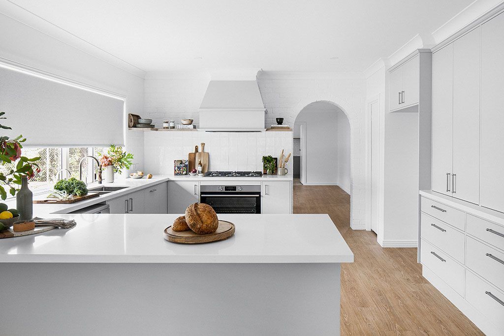a kitchen with white cabinets and hardwood floors and a bread loaf on the counter .