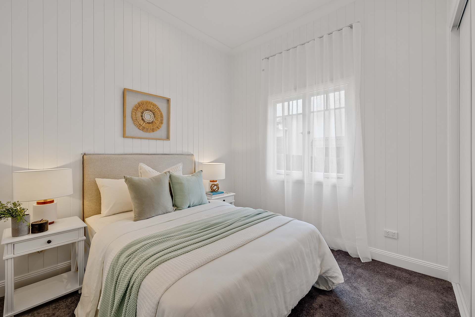 a bedroom with a bed , nightstand , lamps and a window .