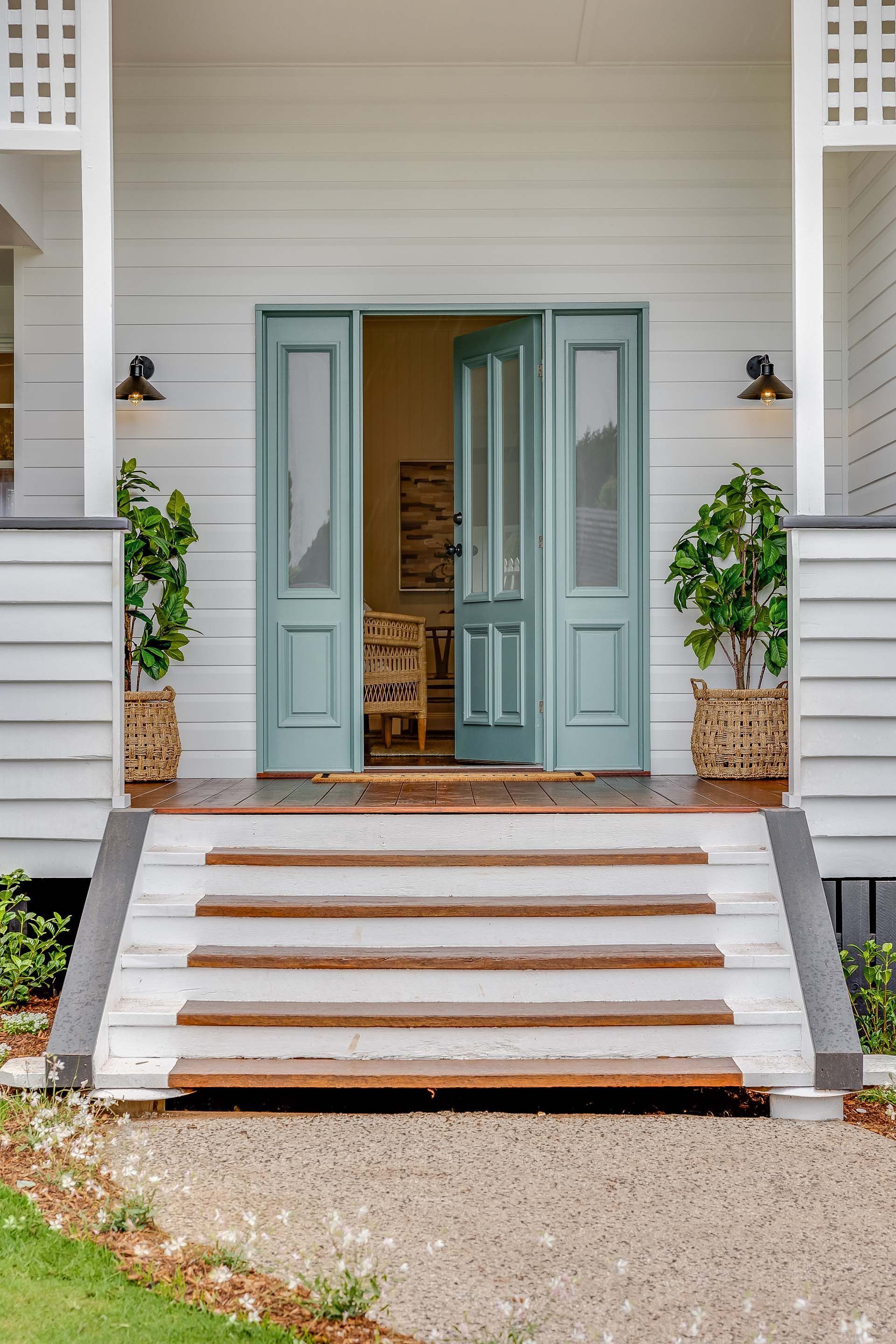 the front door of a white house with blue doors and stairs leading up to it .