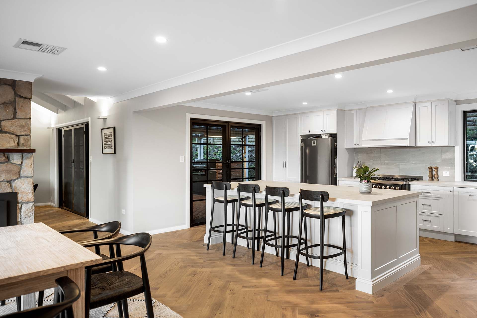 a kitchen with white cabinets , stools , a table and a fireplace .