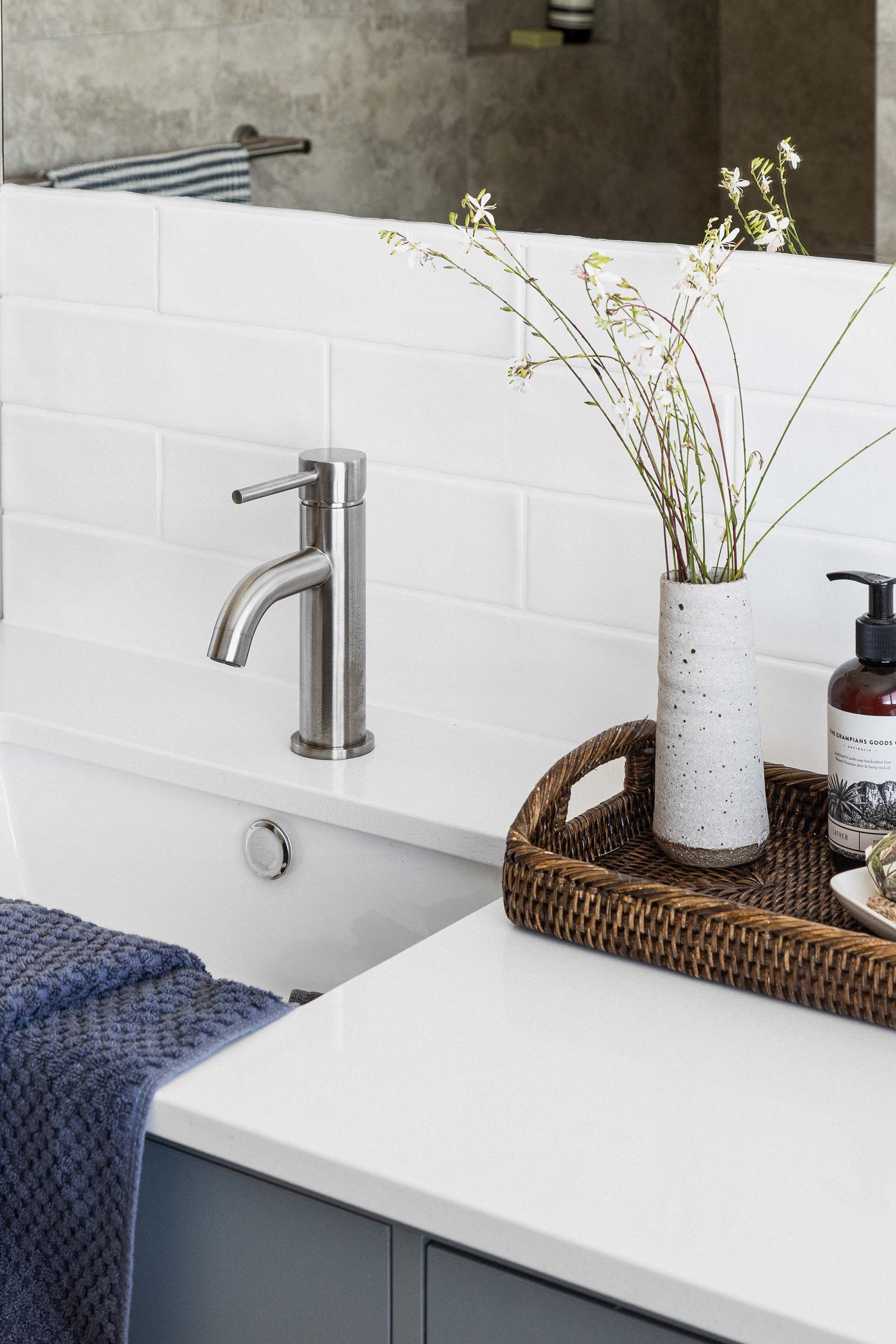 a bathroom with a sink , a vase of flowers and a tray on the counter .