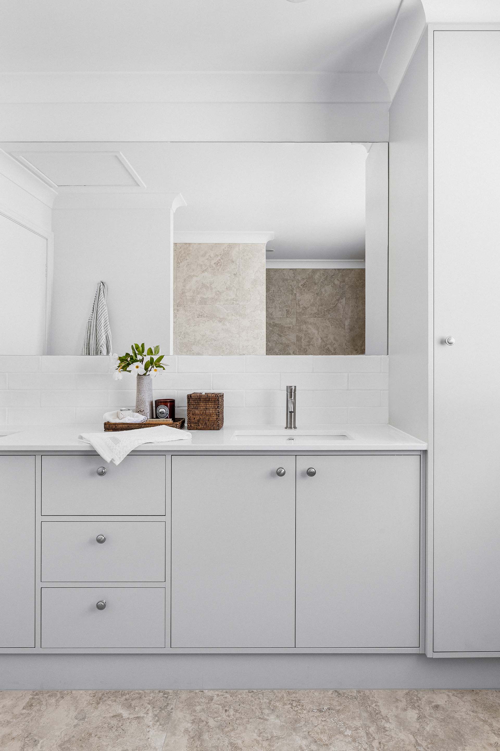 a bathroom with white cabinets , a sink , a mirror and a rug .