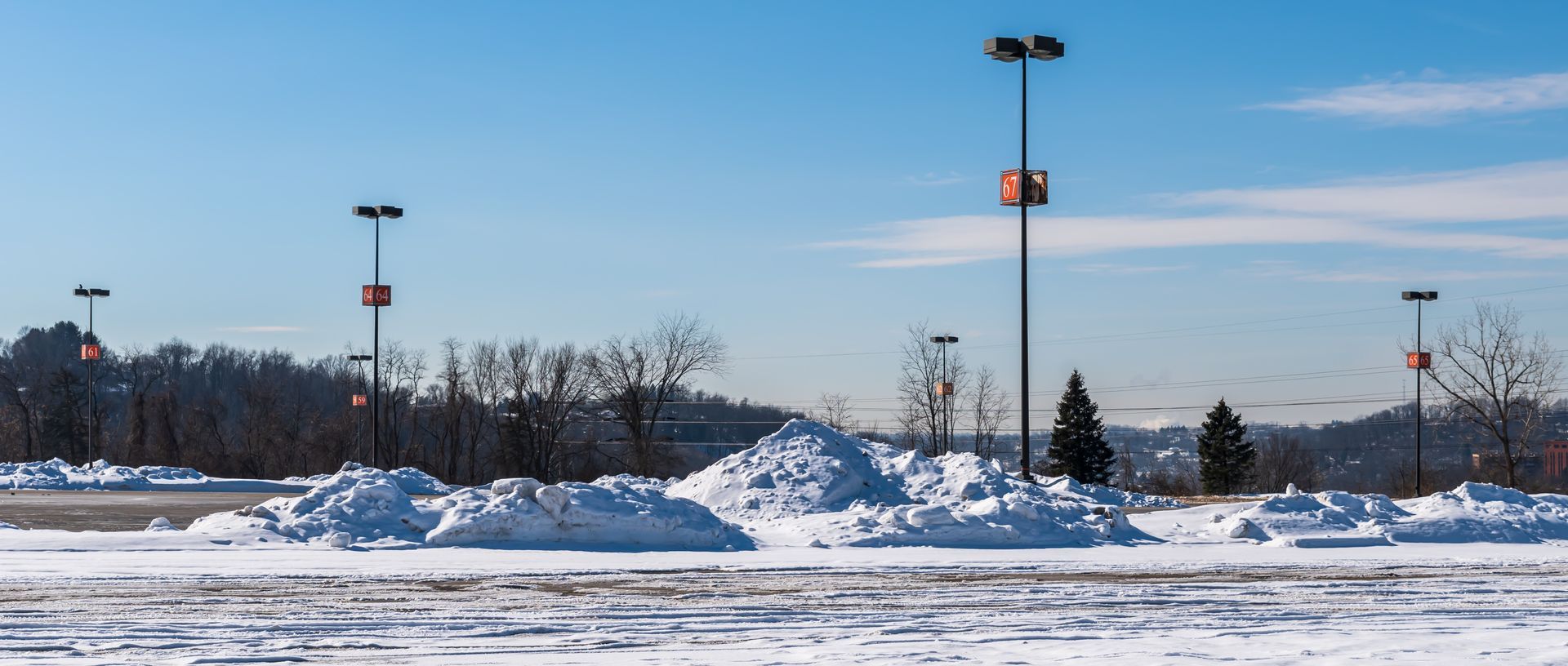 Snow-covered parking lot with tall light poles under a clear blue winter sky.