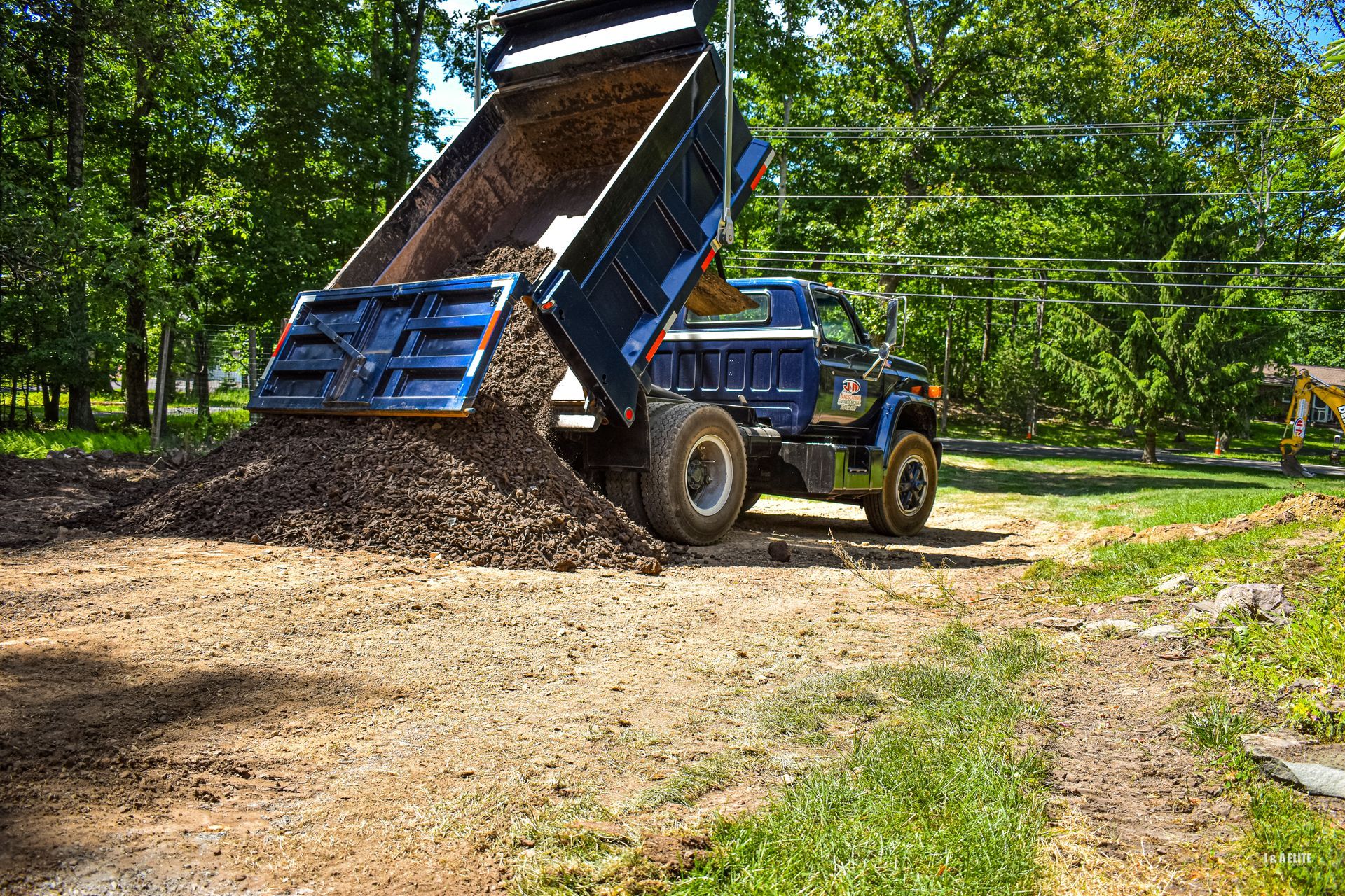 A dump truck is dumping dirt on a dirt road.