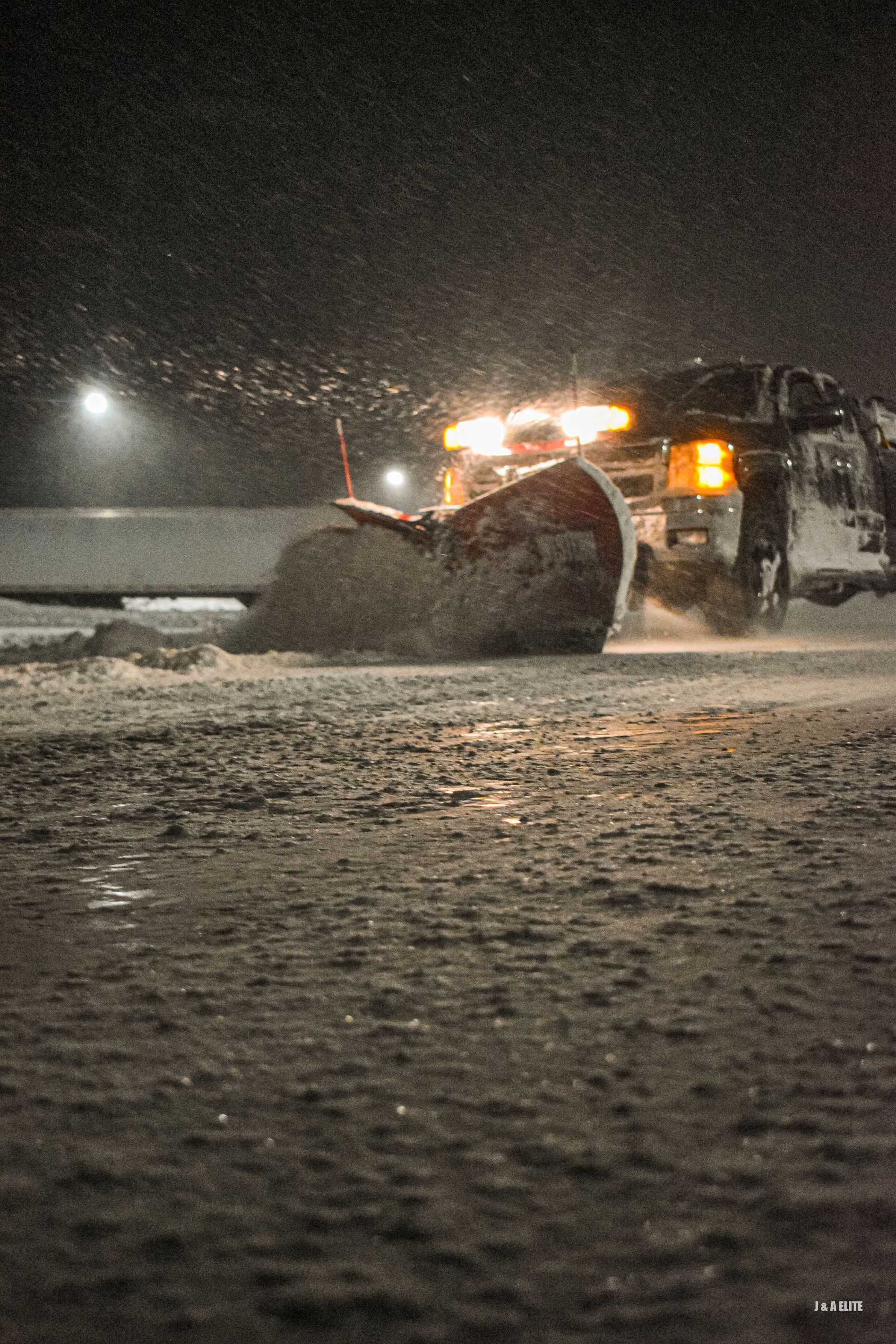 A snow plow is clearing snow from a road at night.