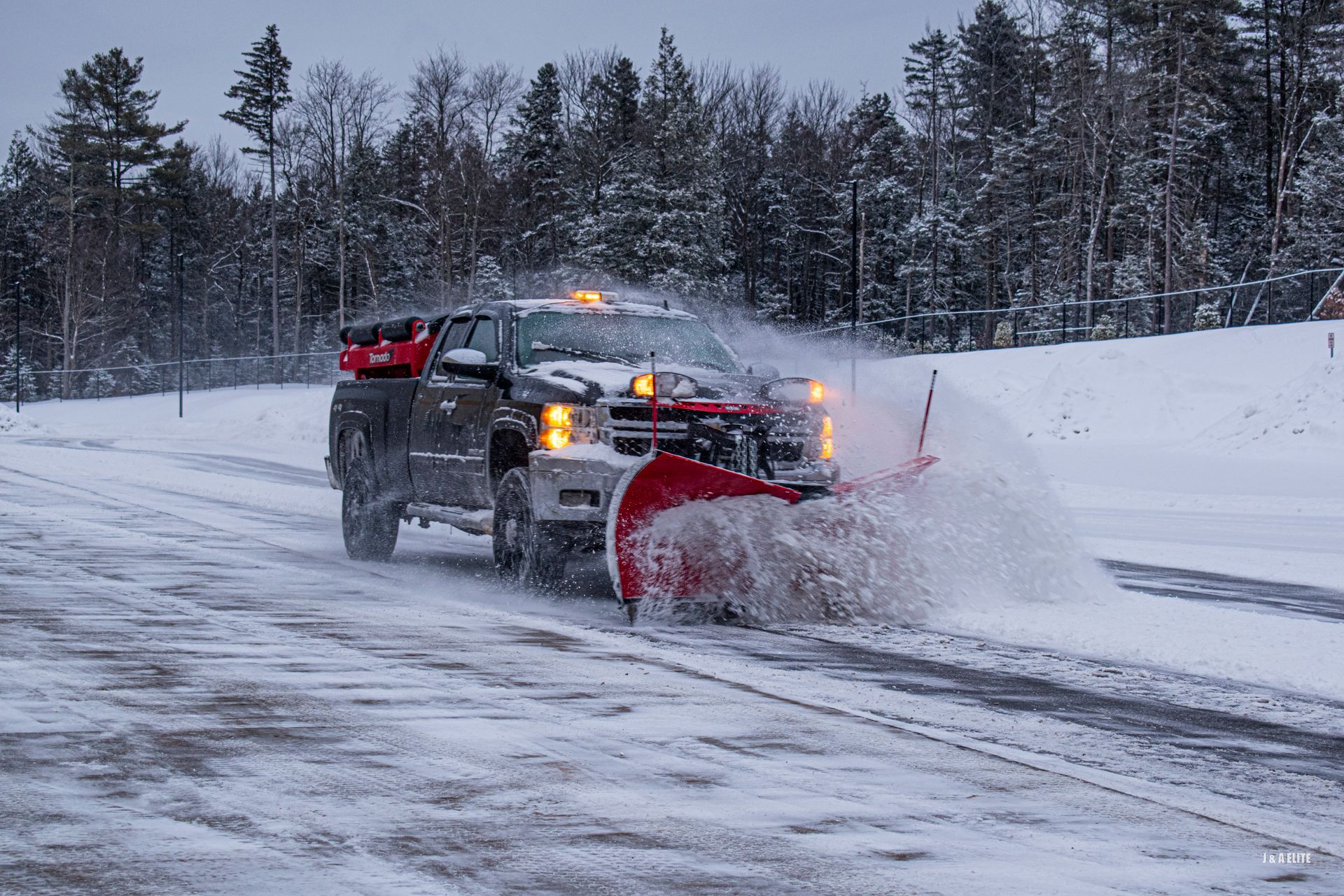 A snow plow is driving down a snow covered road.