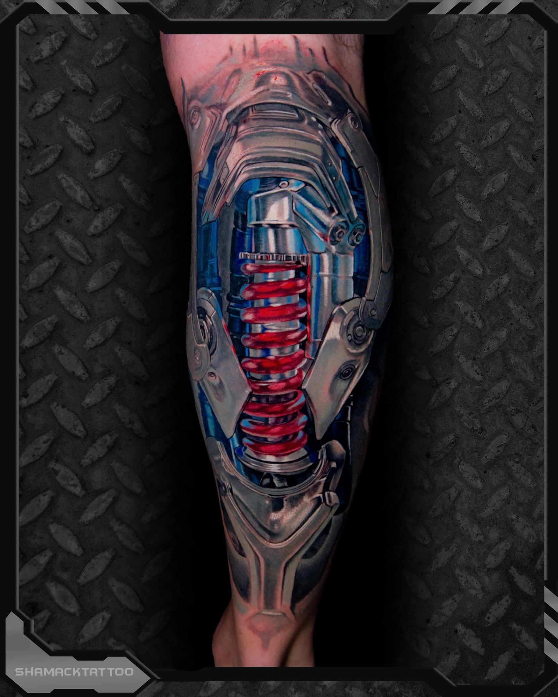 Tattooed forearm with a biomechanical-style tattoo featuring red and blue mechanical details