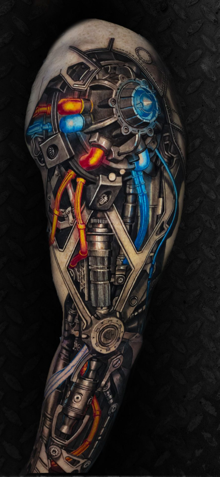 Side view of a tattooed arm with a blue shield tattoo, wearing a black sleeveless shirt and jeans.