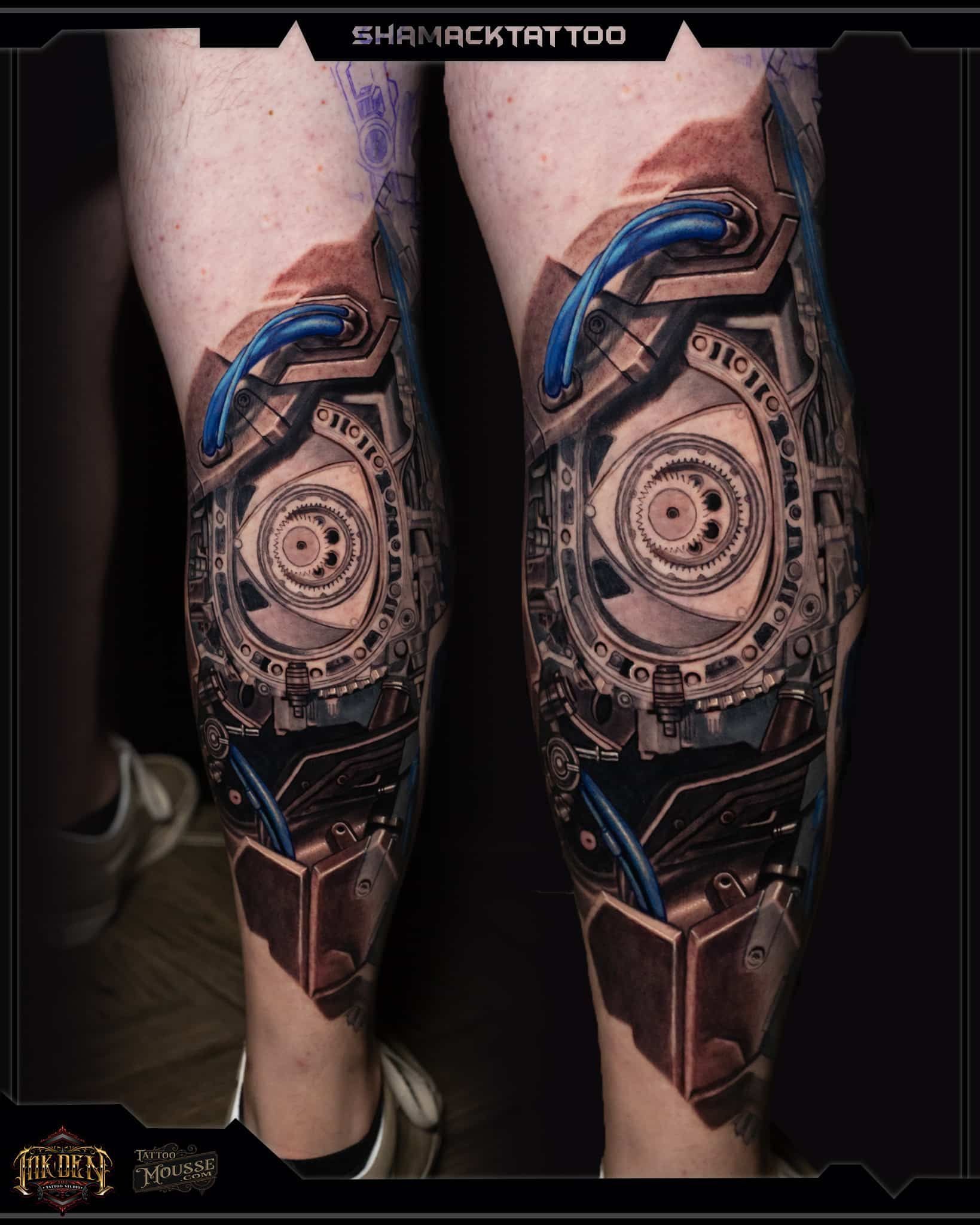 Pair of tattooed lower legs with intricate circular mechanical-style designs and blue accents.