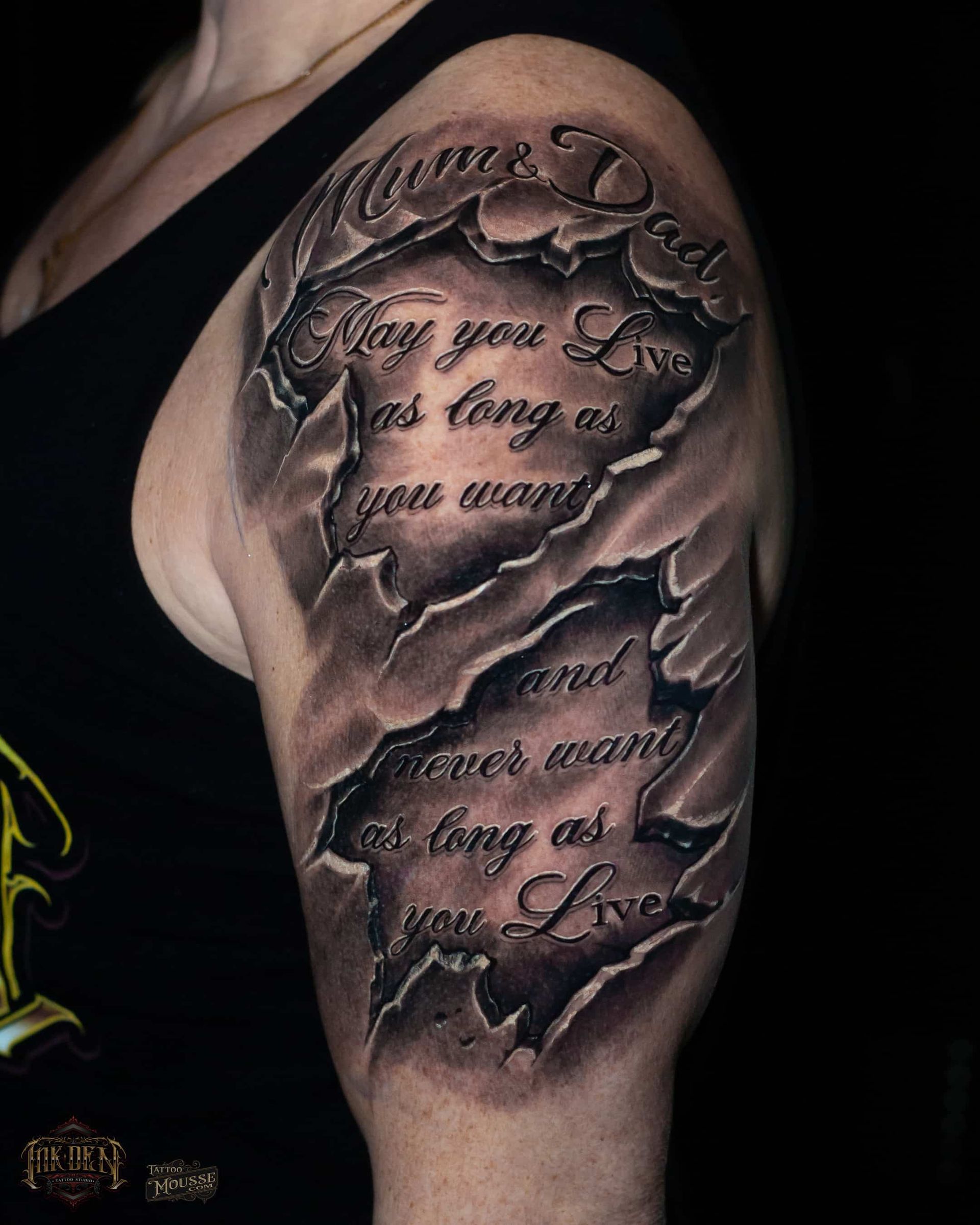 Close-up of a black-and-gray shoulder tattoo with cursive quote text on a muscular arm