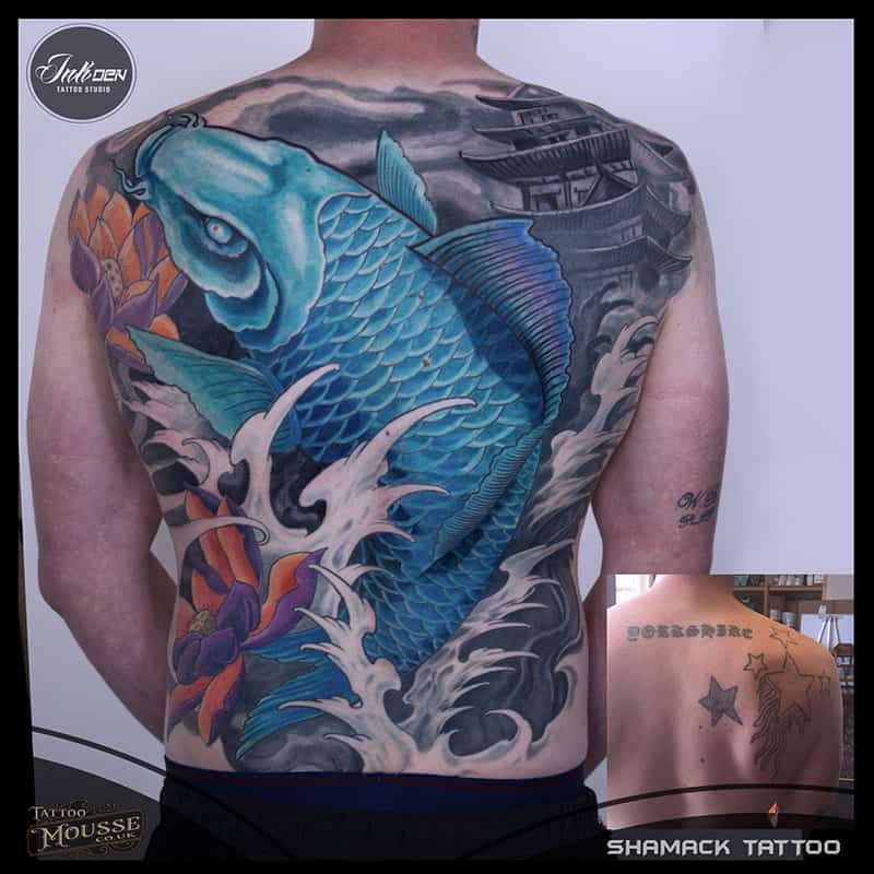 Back tattoo of a large blue fish with black-gray waves and a small inset of a star tattoo on shoulder