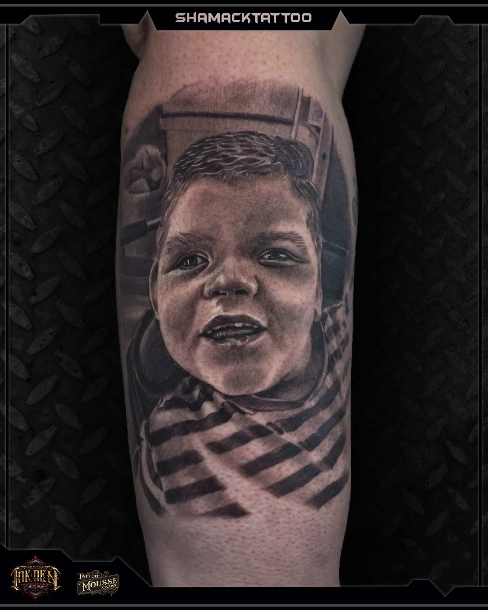 Black-and-gray tattoo portrait of a smiling child on a forearm with geometric patterns beneath it