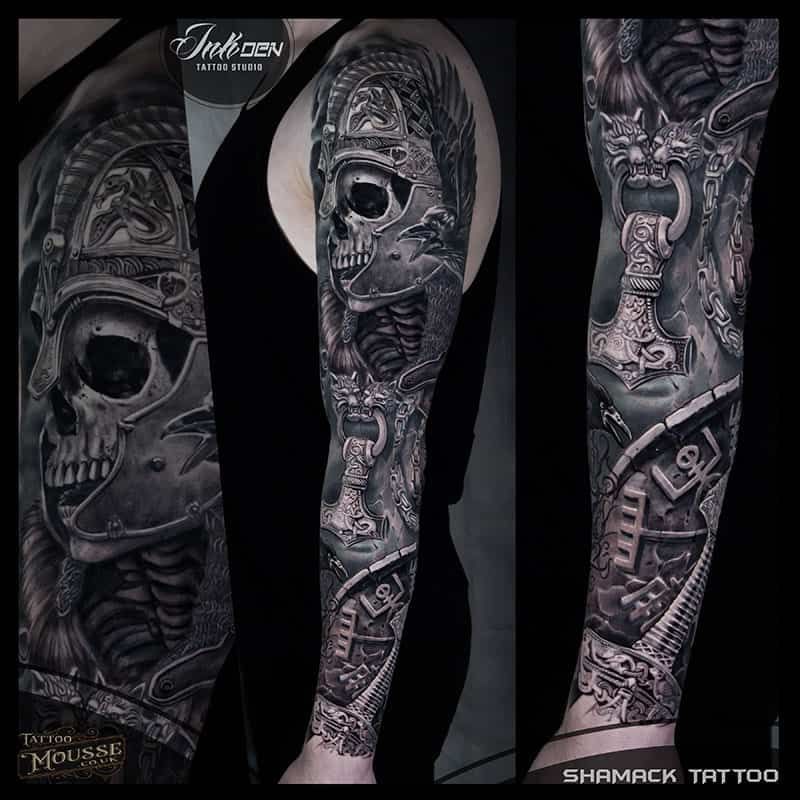 Black-and-gray tattoo sleeve design with carved faces, figures, and dark abstract details on a forearm