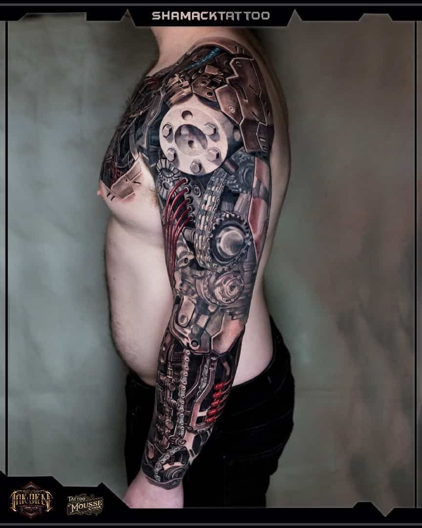 Side view of a person with a large black-and-gray full-sleeve tattoo, wearing dark pants.
