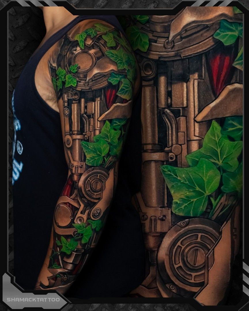 Close-up of tattooed arms with green ivy and steampunk gear designs on a dark background