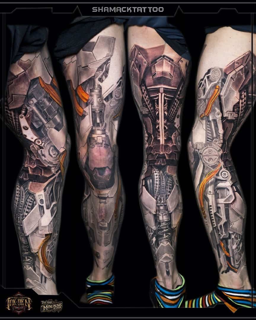 Four tattooed legs with black, gray, and orange biomechanical sleeve designs on a dark background