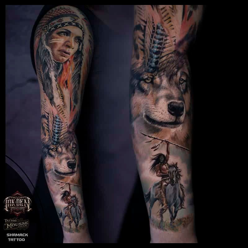 Two tattooed forearms featuring a woman portrait, wolf face, and feathers in black and gray ink
