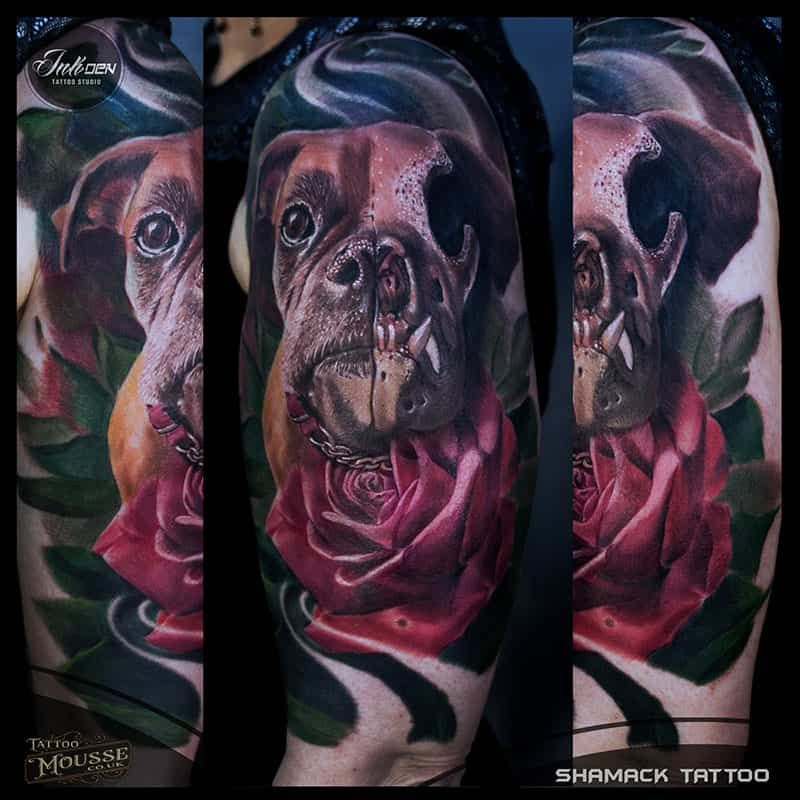 Tattooed dog portrait with a pink rose on a forearm, in rich black, brown, and magenta tones